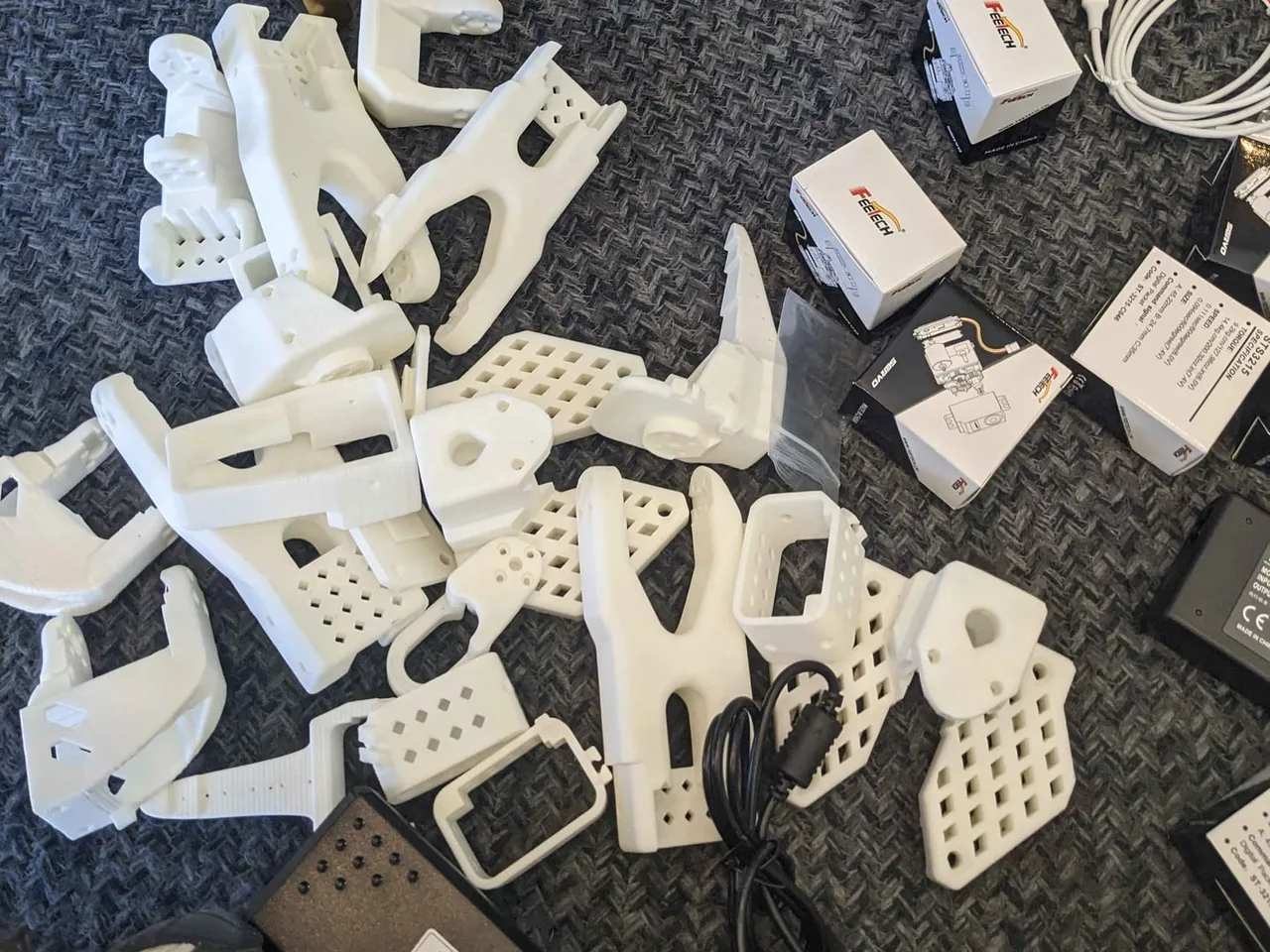 White printed arm links, servos and power supplies spread across the carpet