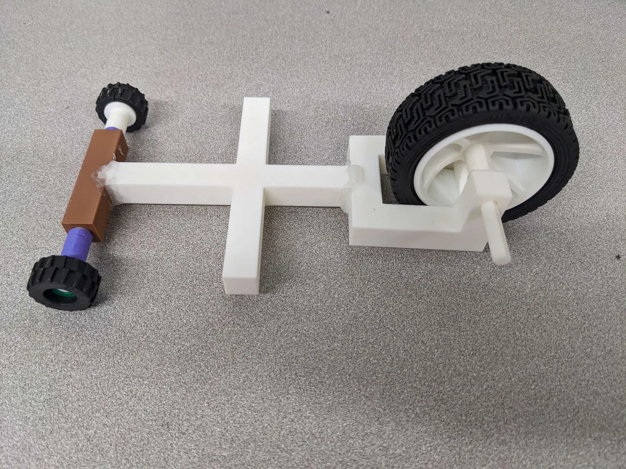 A white printed vehicle frame with two small front wheels and one large rear wheel, before fitting rubber bands