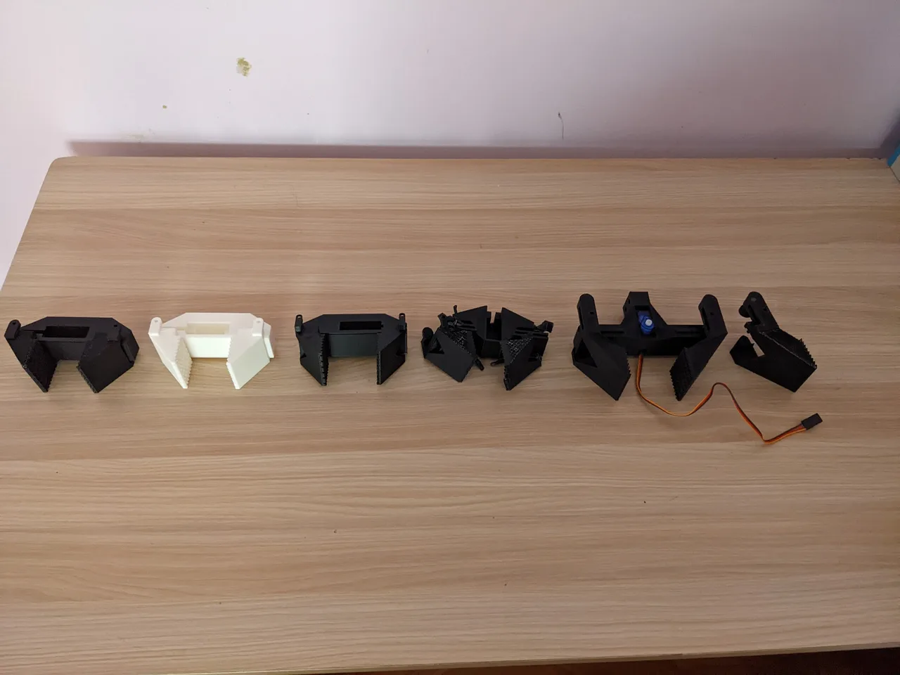 Six printed gripper revisions lined up on a table, including servo-equipped versions and a damaged print