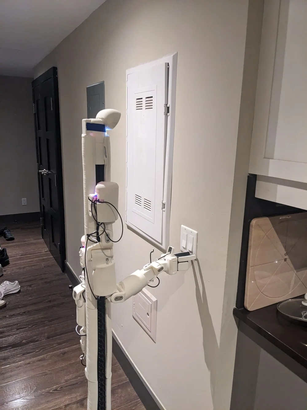 BracketBot in the apartment with its wrist camera and gripper beside a wall switch