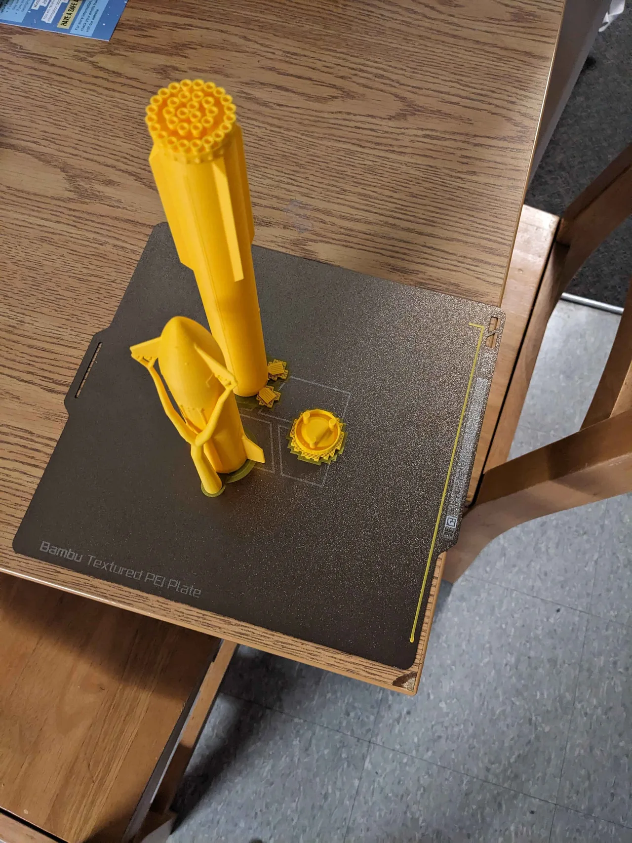 A tall yellow supported print with separate parts beside it on the build plate
